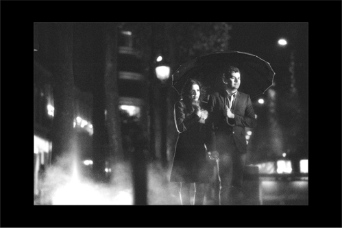 Engaged couple walking on cold and rainy Paris streets in the evening